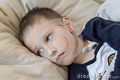 Pre-school sick boy lying in bed with a thermometer. Ill boy doesnâ€™t feel well. - Image Stock Photo